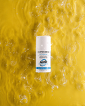 A white cylindrical bottle of APP Labs 4% Peptide Complex serum, surrounded by splashing water droplets on a vibrant yellow background.