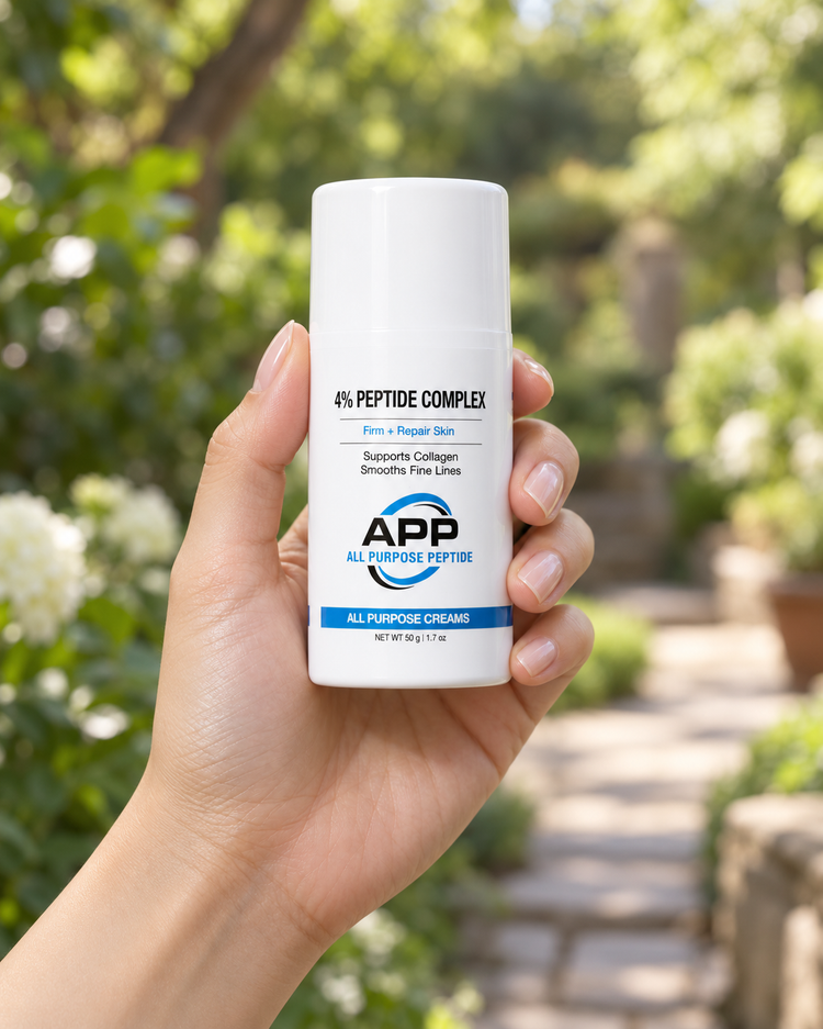 A hand holding a white bottle of APP All Purpose Peptide cream against a blurred green garden background.